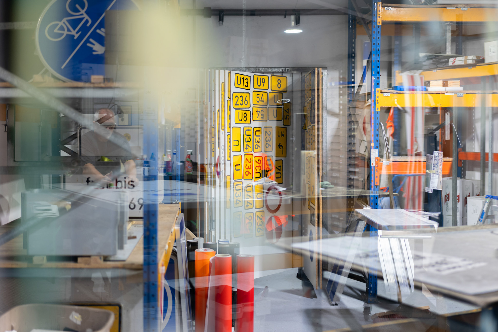 Blick auf ein Lager mit verschiedenen Verkehrsschildern und Regalen voller Materialien in einer Werkstatt.