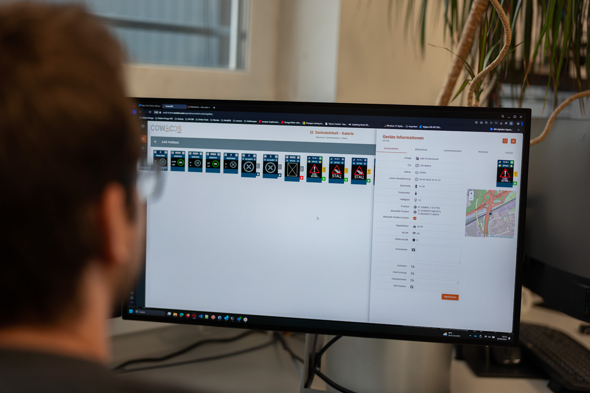 Monitor mit der cowacos-Benutzeroberfläche, die verschiedene Verkehrssignale und Informationen anzeigt, während eine Person im Hintergrund arbeitet.