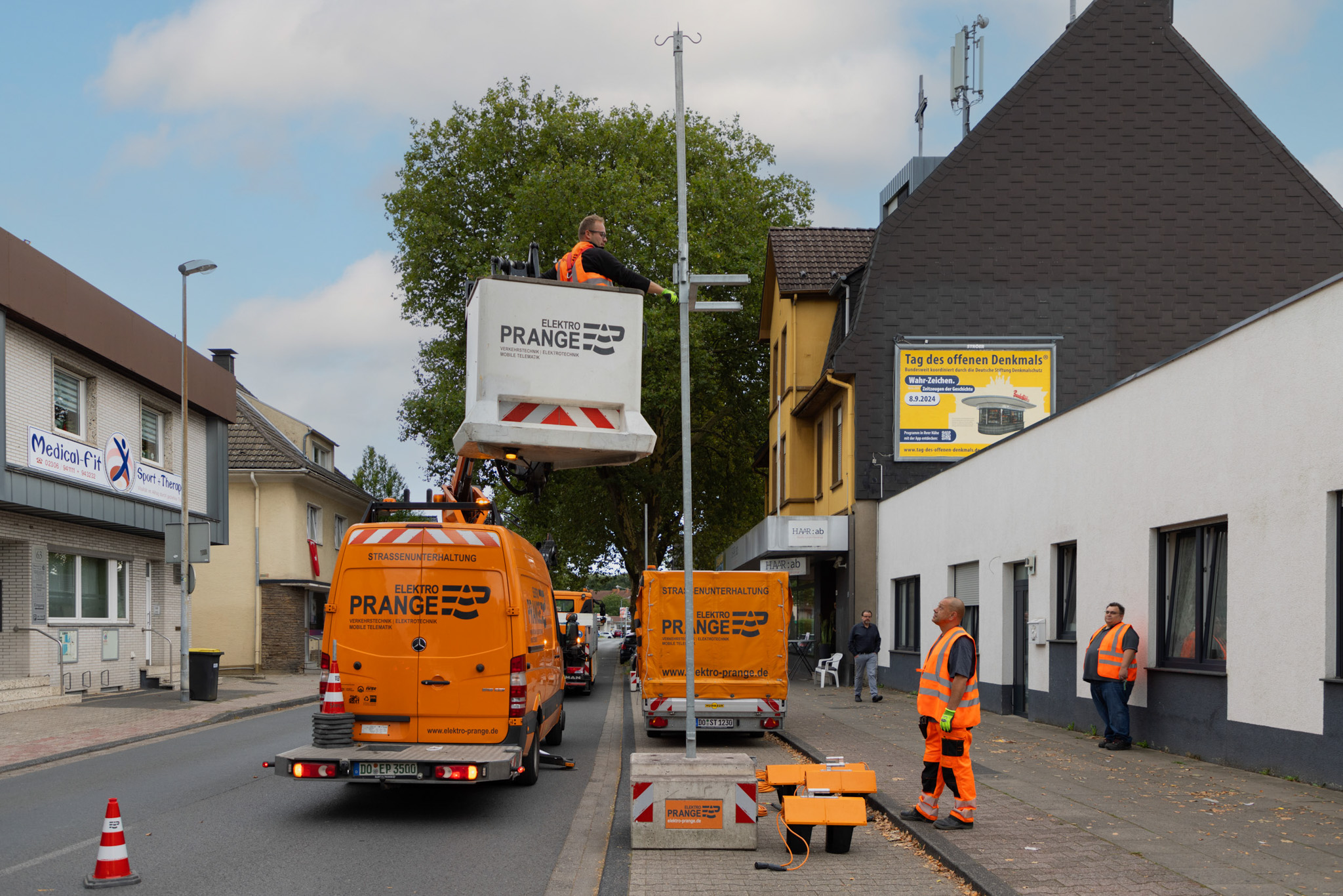 Mitarbeiter von Elektro Prange in orangefarbener Arbeitskleidung, der eine Hebebühne bedient, um eine Ampelanlage aufzubauen.