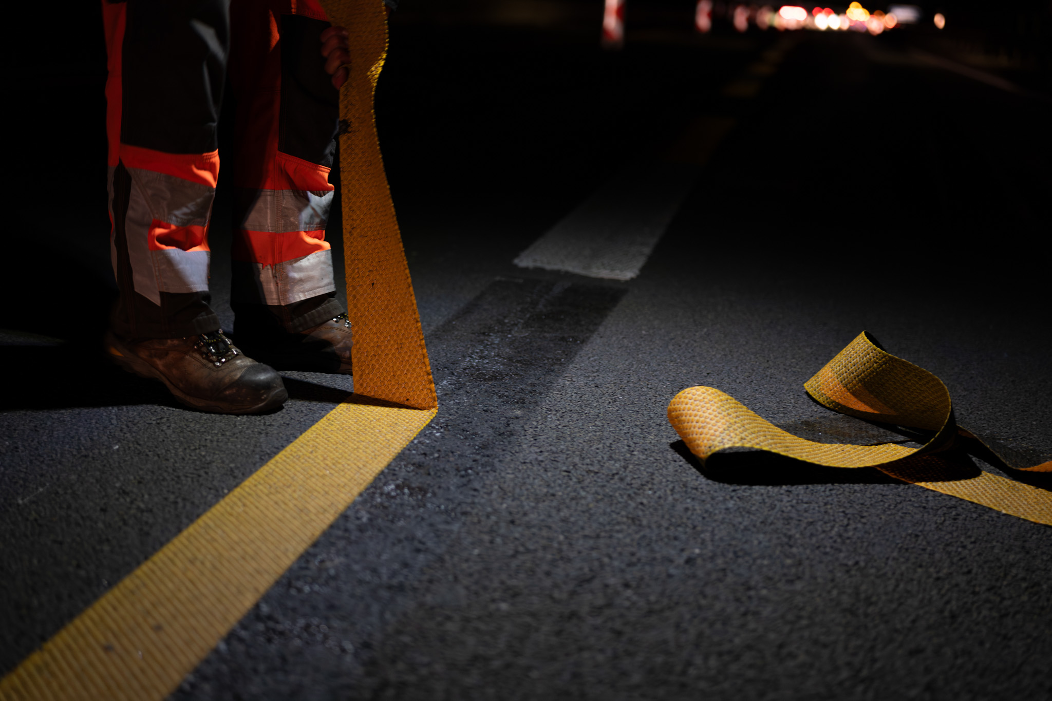Eine Person entfernt eine gelbe, temporäre Fahrbahnmarkierung auf der Autobahn.