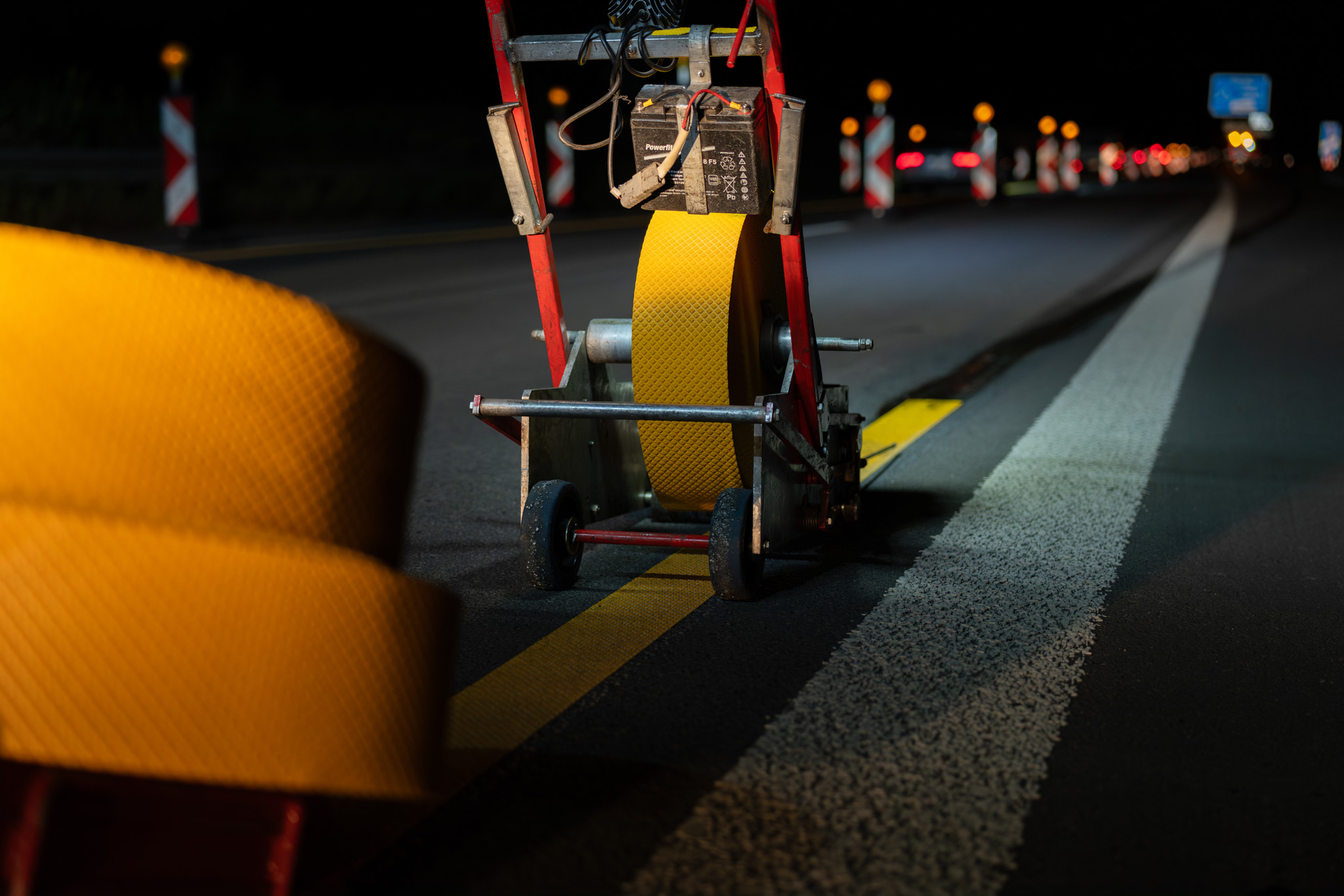Maschine zur Markierung von Straßen mit gelbem reflektierendem Material auf einer Fahrbahn bei Nacht.