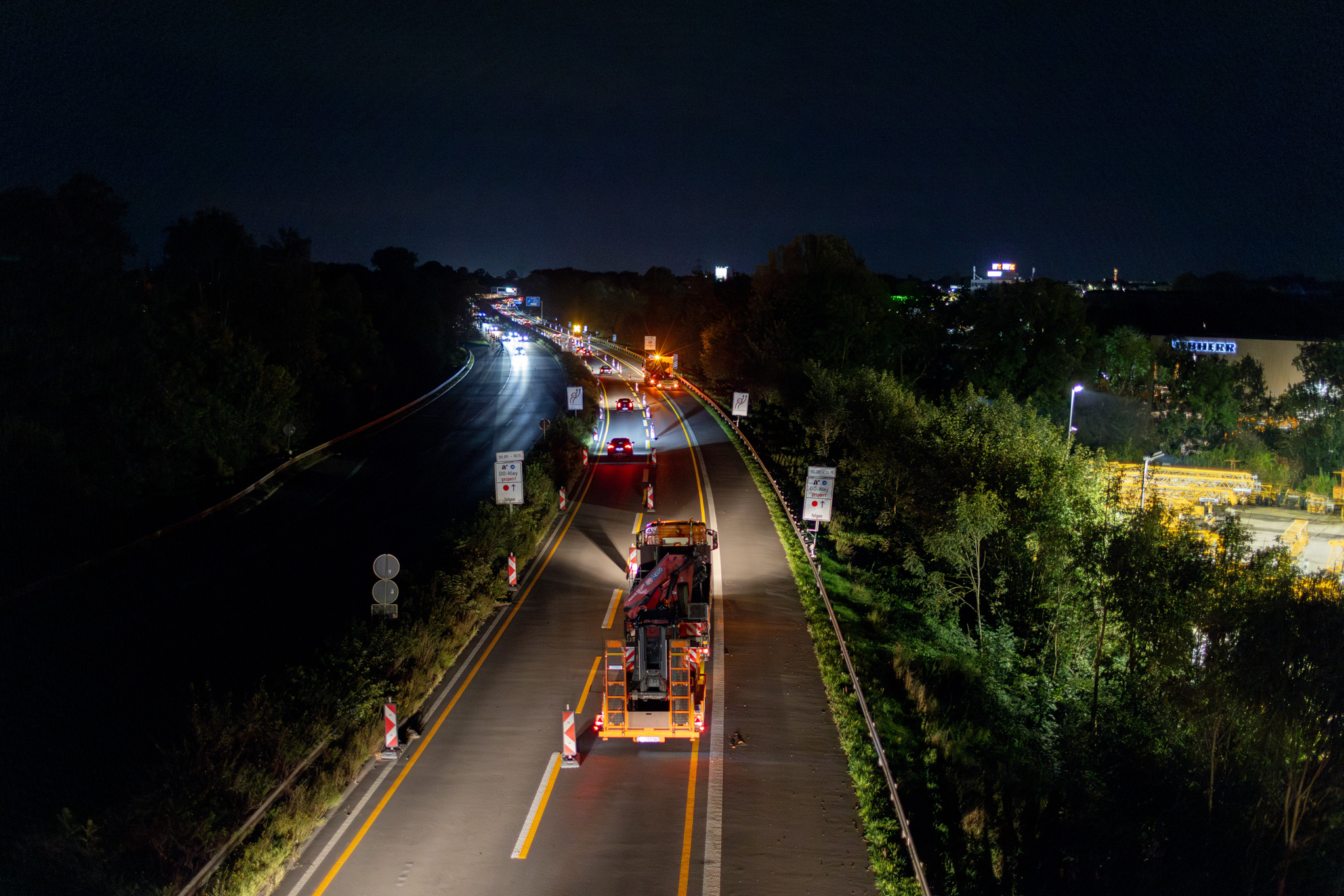 Bauarbeiten auf einer Autobahn bei Nacht mit Baustellenfahrzeugen und Warnlichtern, die den Verkehrsfluss leiten.