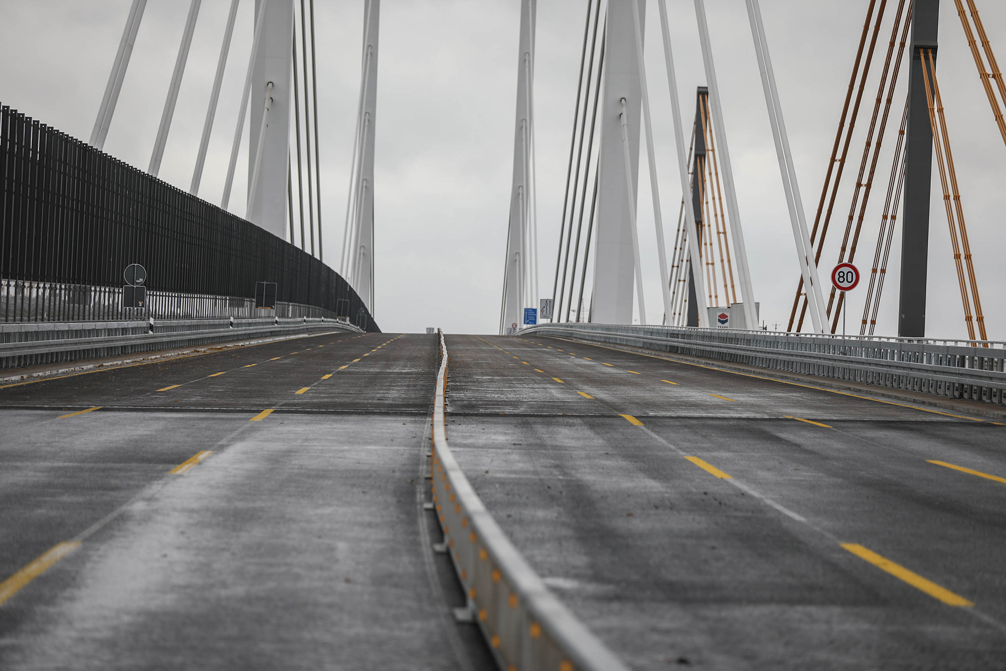 Leere Straße auf einer modernen Brücke mit auffälligen Stützpfeilern und Fahrbahnmarkierungen.