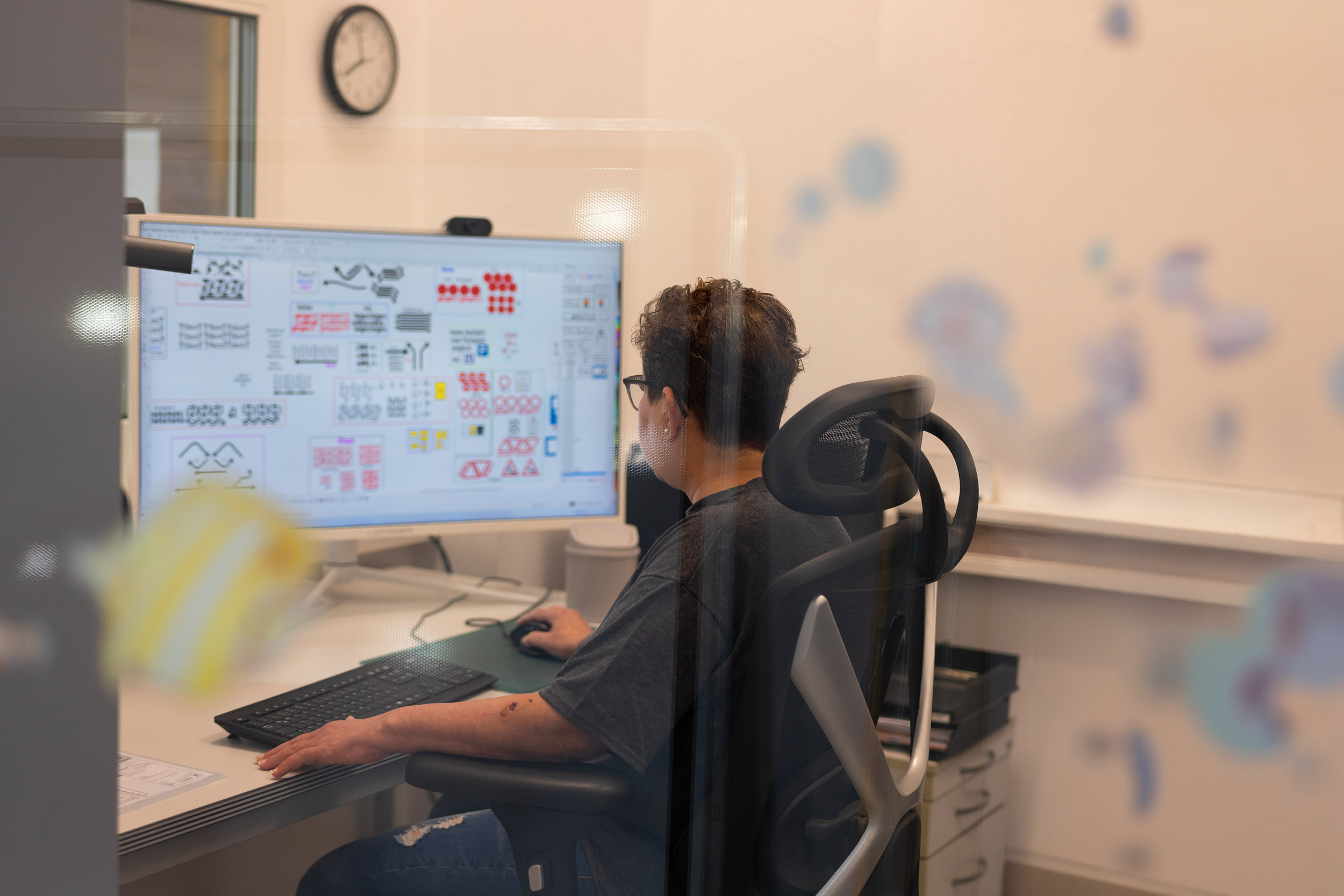 Person sitzt an einem Schreibtisch und arbeitet an einem Computer mit verschiedenen grafischen Designs auf dem Bildschirm.