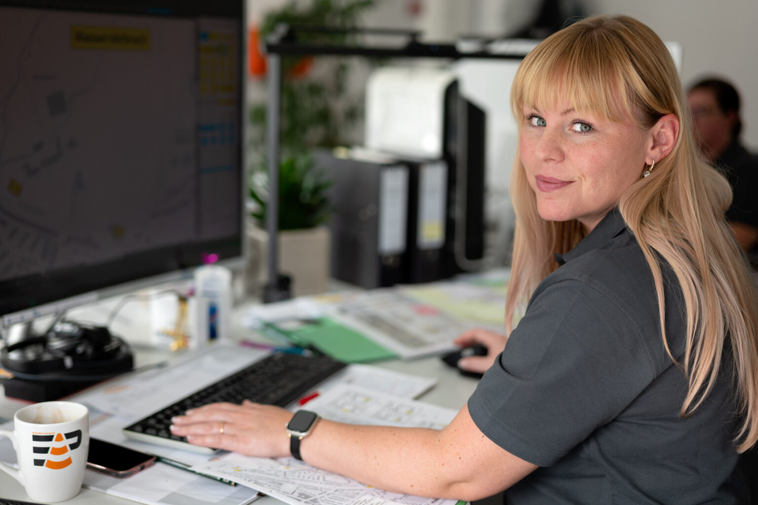 Eine Frau sitzt vor einem großen Bildschirm auf dem Verkehrspläne zu sehen sind.